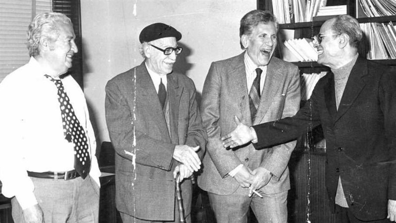 توفيق الحكيم وسط زملائه الكتاب يرتدى البريه ويمسك بالعصا