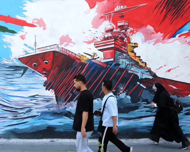 إيرانيون يسيرون أمام جدارية في طهران