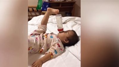 لقطات طريفة لطفلة تستخدم قدمها لحمل زجاجة الحليب (فيديو)