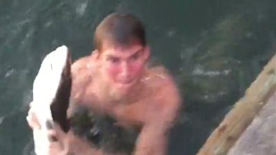 بالفيديو والصور.. شاب يقفز في المياه ليصطاد سمكة قرش بيديه العاريتين